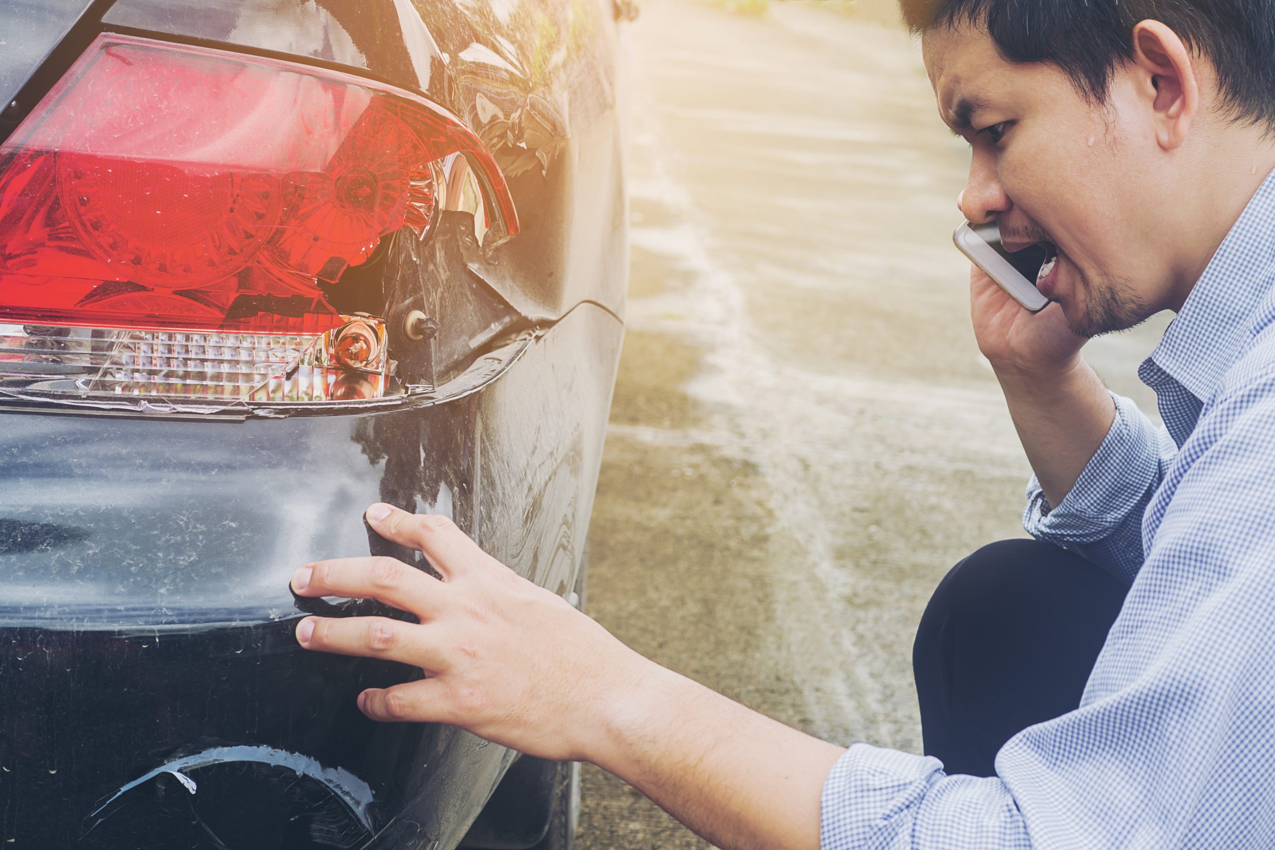 man calling his insurance company while inspecting the damage on his car