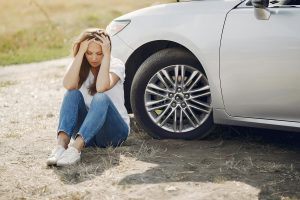 stressed woman sitting next to a broken-down car