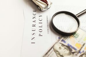 dollar bills, a magnifying glass, and a toy classic car placed on top of an insurance policy document